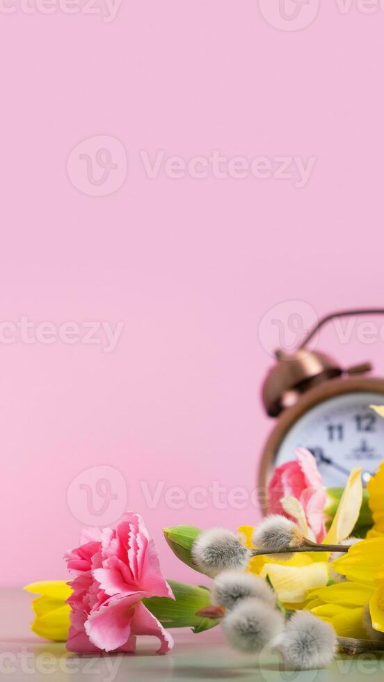 Spring flowers with defocused alarm clock. Spring time, daylight savings concept, spring forward. Copy space. photo