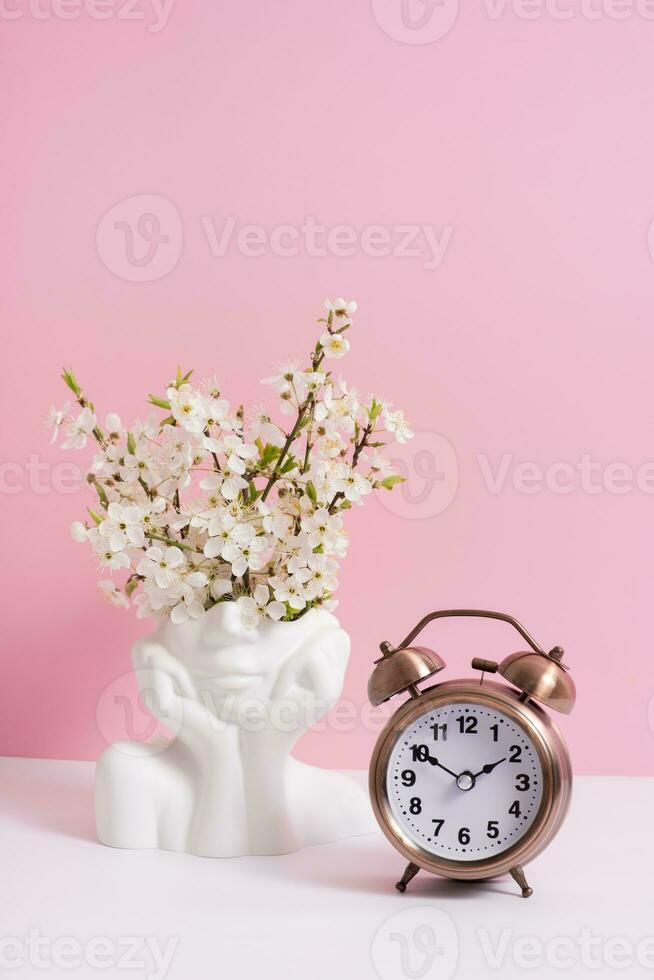 Alarm clock and head shape vase with spring bloom flowers on pink background photo