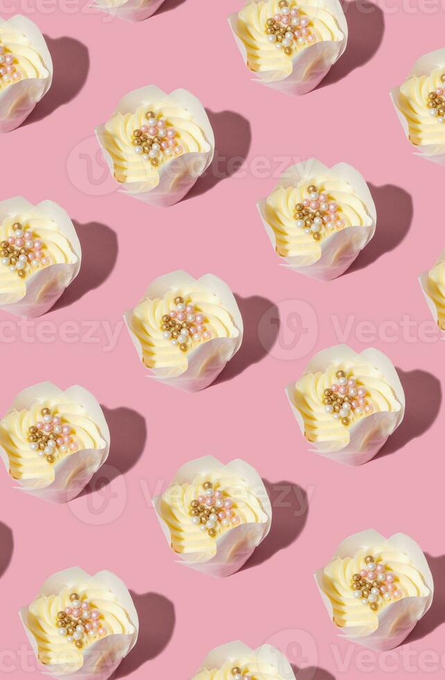 Pattern made from cupcakes with cream and decorating on pink background. Sweet food pattern. photo