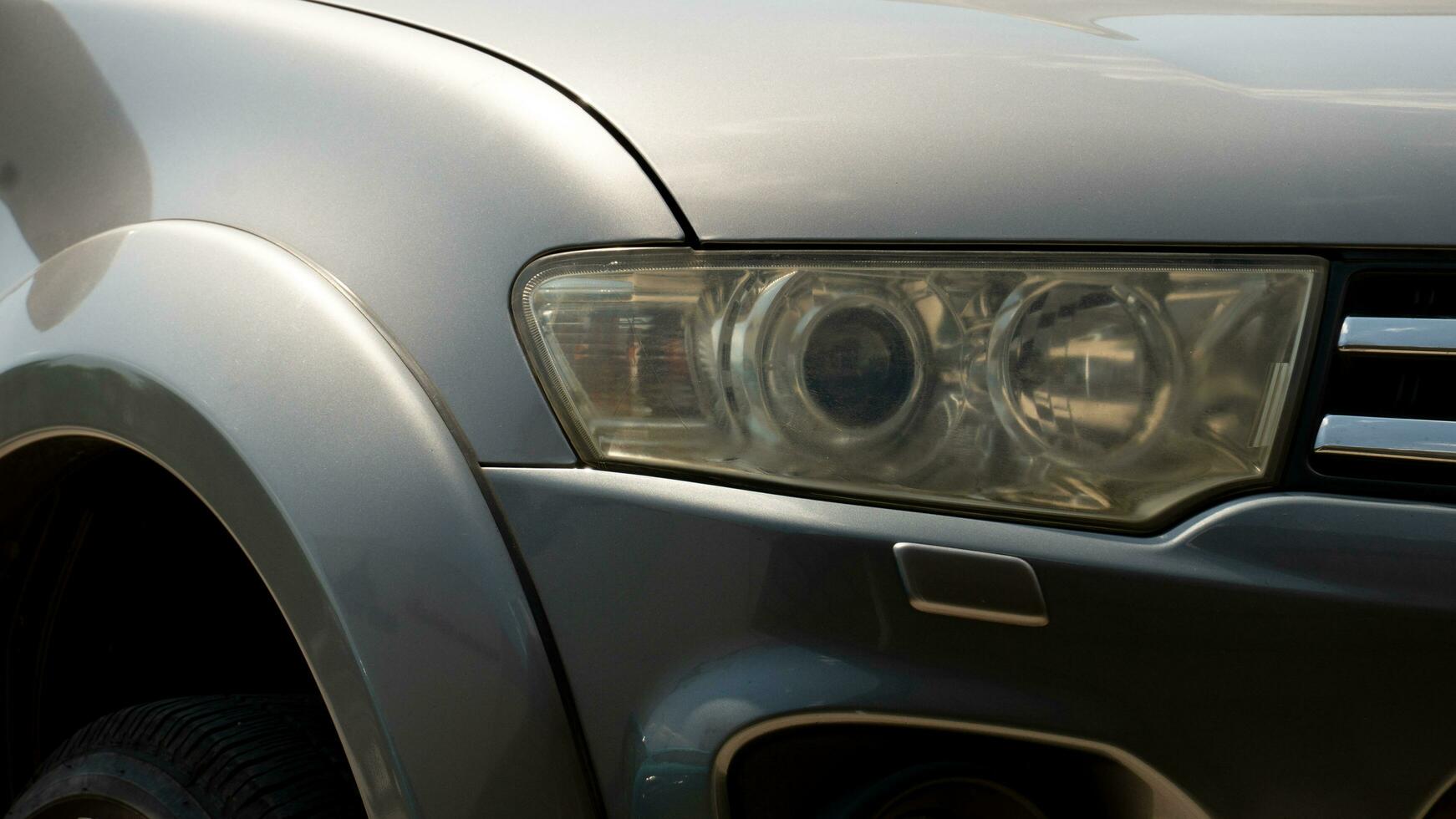 faros son antiguo y aburrido de gris coche. coche parque en el estacionamiento zona debajo luz de sol. foto