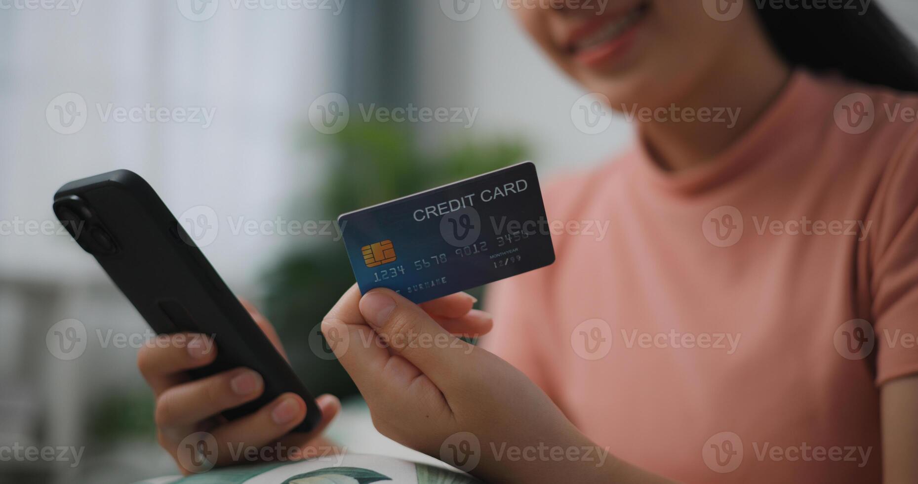 retrato cerca arriba de joven asiático mujer sentado en sofá en vivo habitación, hace en línea bancario pagos mediante el Internet desde banco tarjeta en teléfono inteligente ,compras en línea con crédito tarjeta. foto