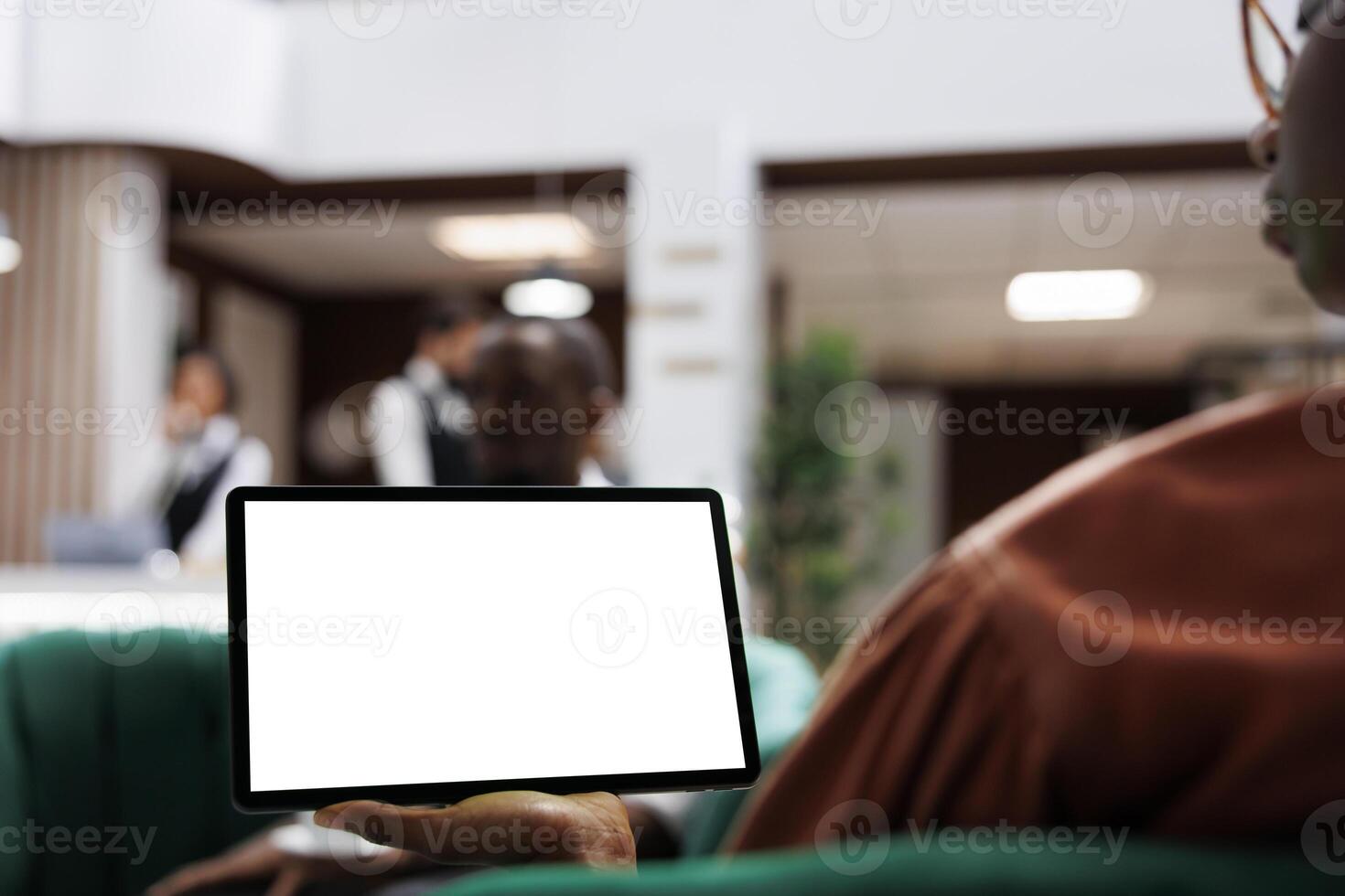 Female guest holding device at reception, relaxing in lounge area with digital tablet and blank screen template. Woman using white display with isolated copyspace at front desk lobby. photo