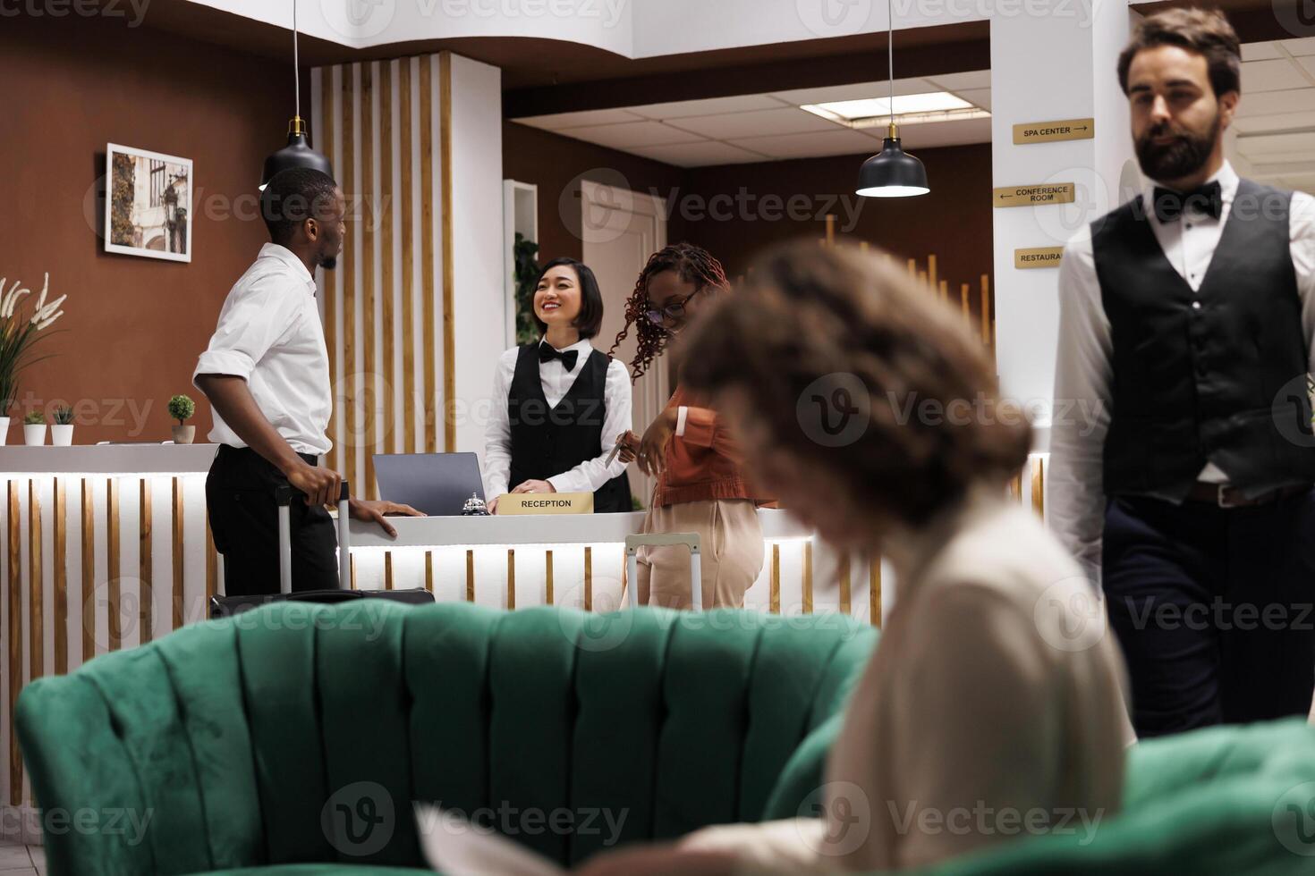 Man welcoming people at front desk, providing excellent service with registration at hotel. Male reception worker talking to guests in lobby, looking to book room at resort upon their arrival. photo