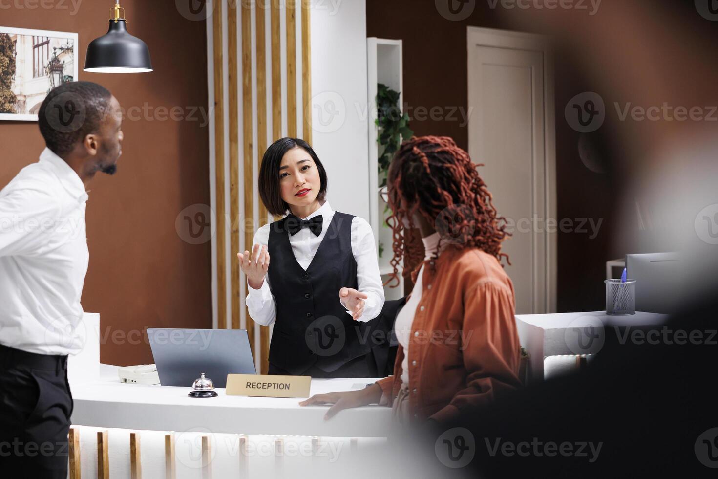 Worker talking to couple at reception desk in lobby, providing luxury service to guests. Asian receptionist welcoming people at modern expensive hotel, doing registration at entrance. photo