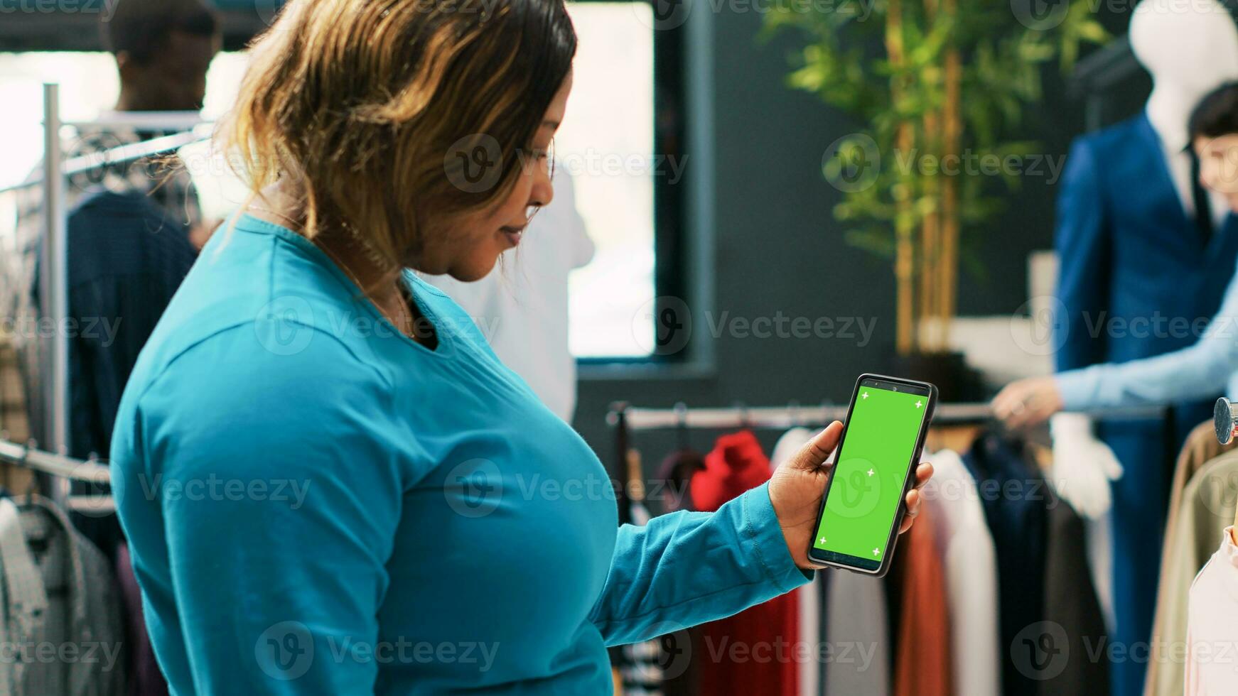 africano americano cliente participación móvil teléfono con verde pantalla mostrar, comprobación ropa Tienda aplicación elegante mujer compras para de moda ropa y de moda accesorios en moderno boutique foto