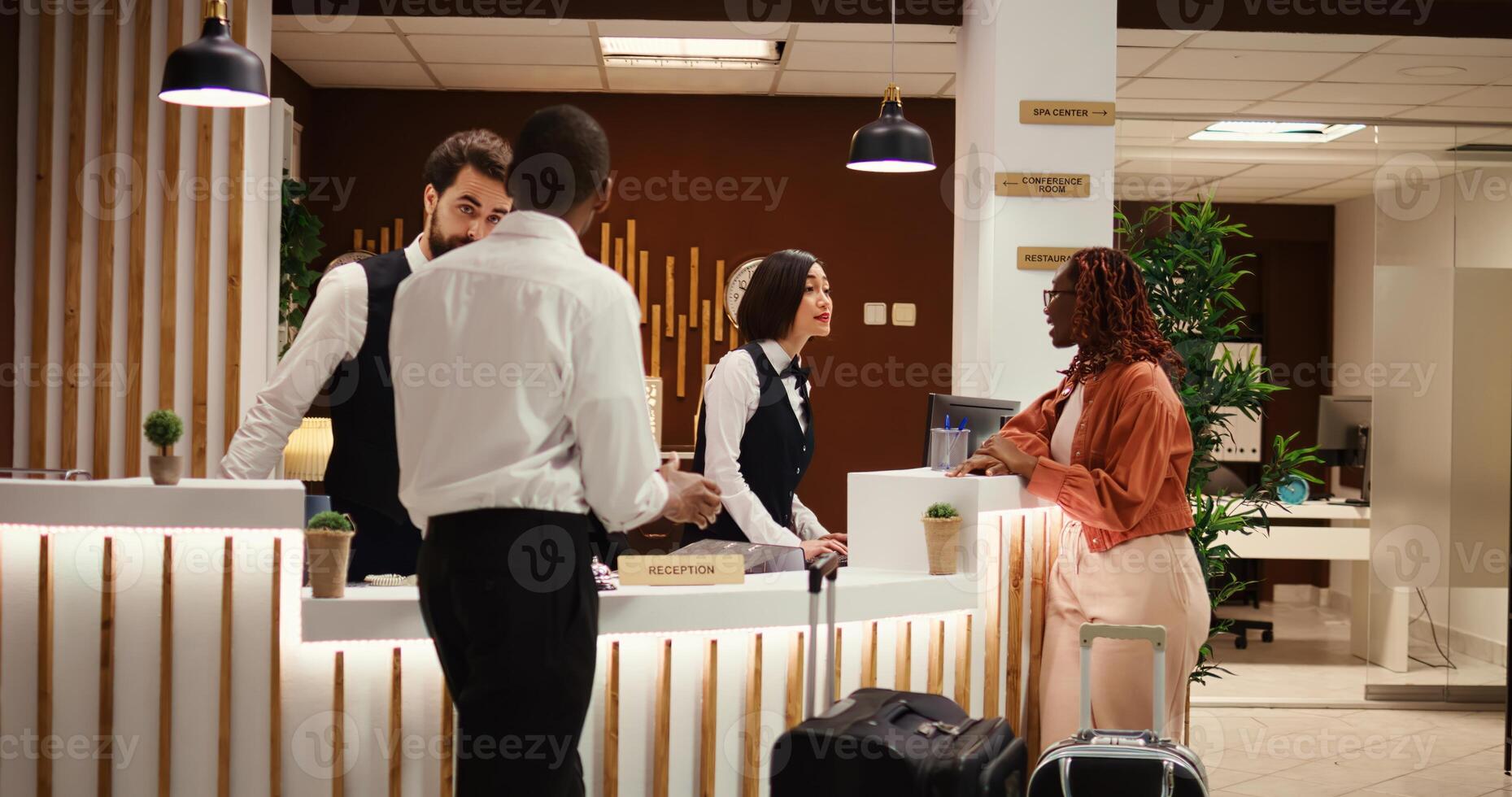 Friendly smiling concierge personnel assisting tourists with room registration. Cheerful front desk receptionists answering customer inquiries about hotel amenities during guests check in process photo