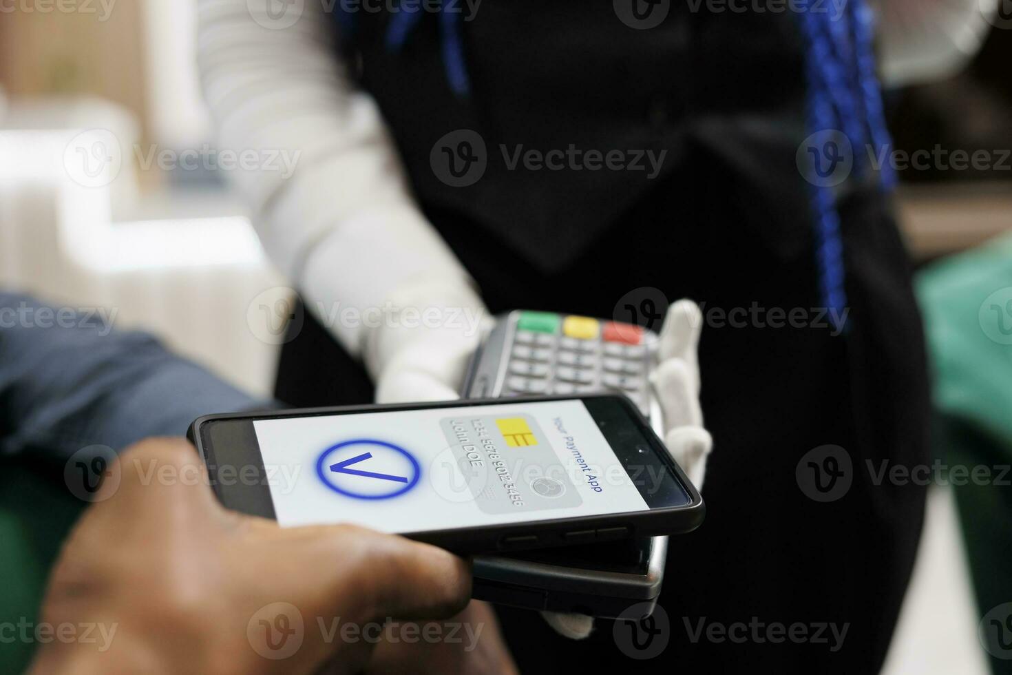Waiter holding POS terminal accepting cashless transaction from customer in restaurant or hotel. Client paying with phone, making mobile payment, using NFC payment app, close up photo