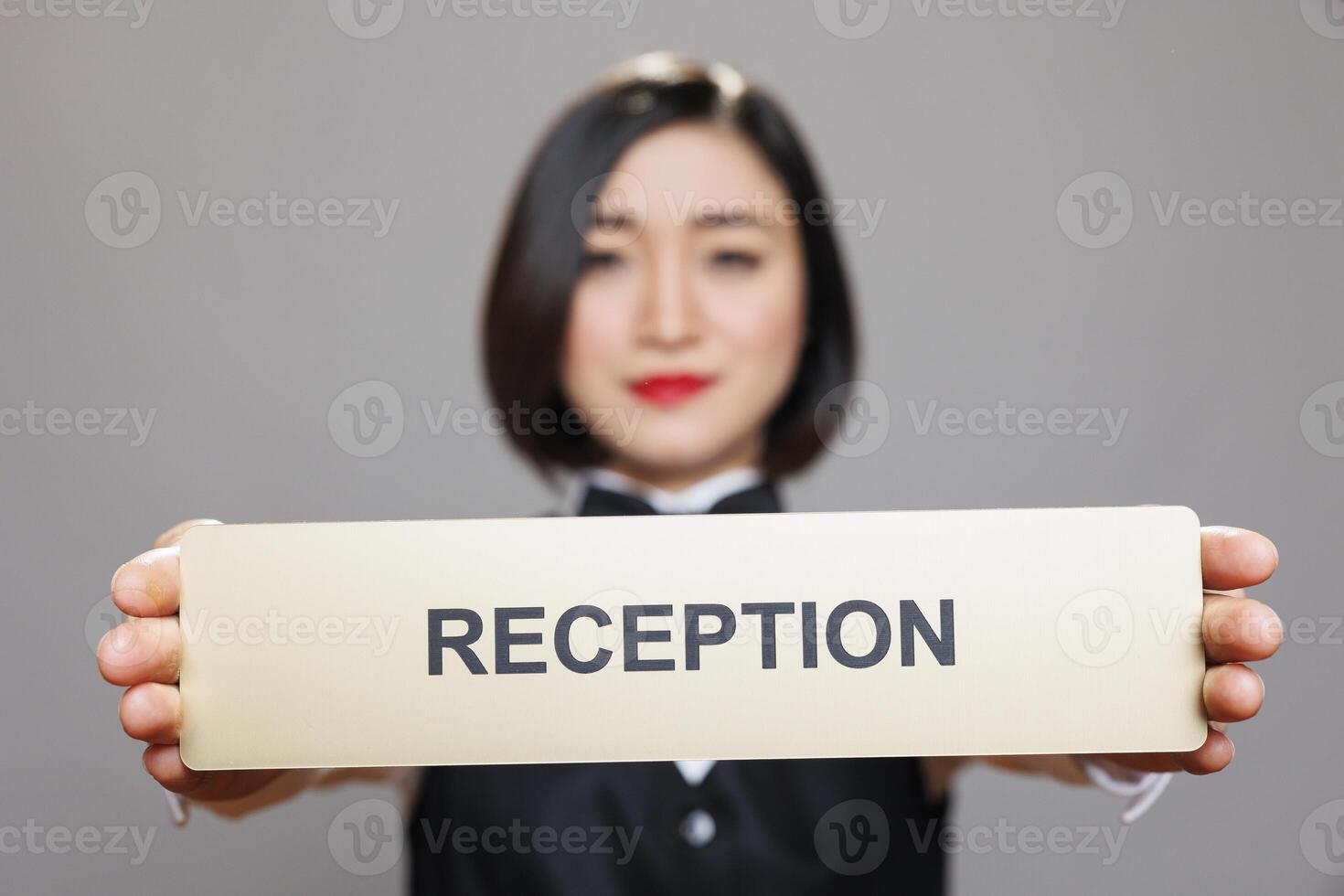 Professional asian waitress holding in hands tabletop reception plate portrait. Restaurant woman administrator in uniform showing receptionist steel signage and looking at camera photo