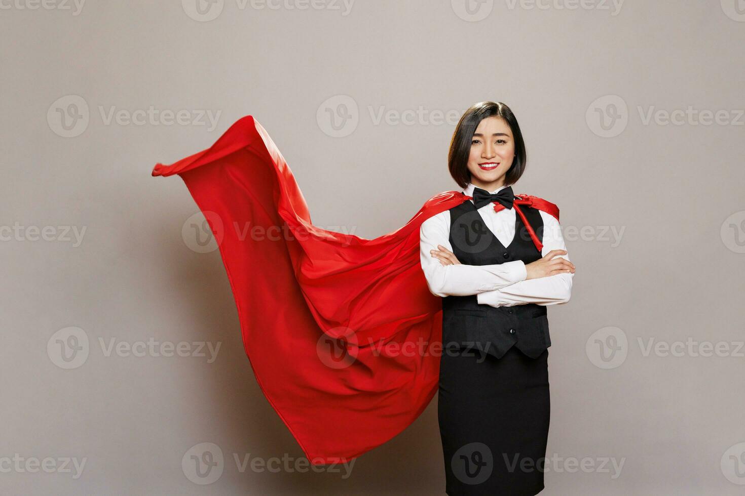 confidente sonriente camarera vistiendo superhéroe rojo capa, demostración fuerza y fuerza. abastecimiento Servicio alegre mujer trabajador en uniforme y supermujer capa en pie con doblada manos retrato foto