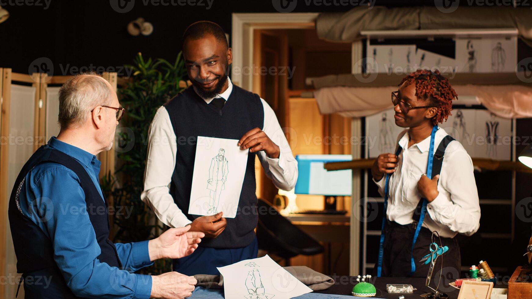 Customer discussing about sizes with senior couturier and assistant to design suit, woman taking measurements with meter. Measuring tape and manufacturing tools in atelier workshop. photo