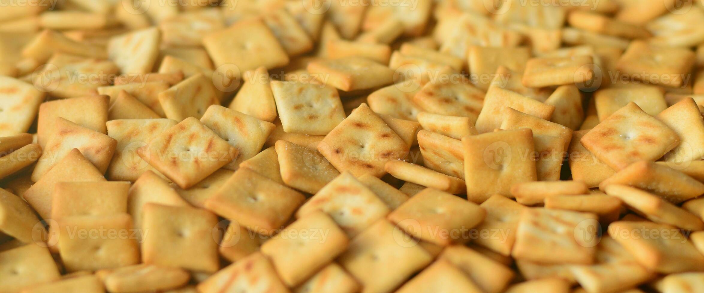 A lot of small cookies are square shaped. A pattern of a yellow salt cracker. Background image with salted pastry photo