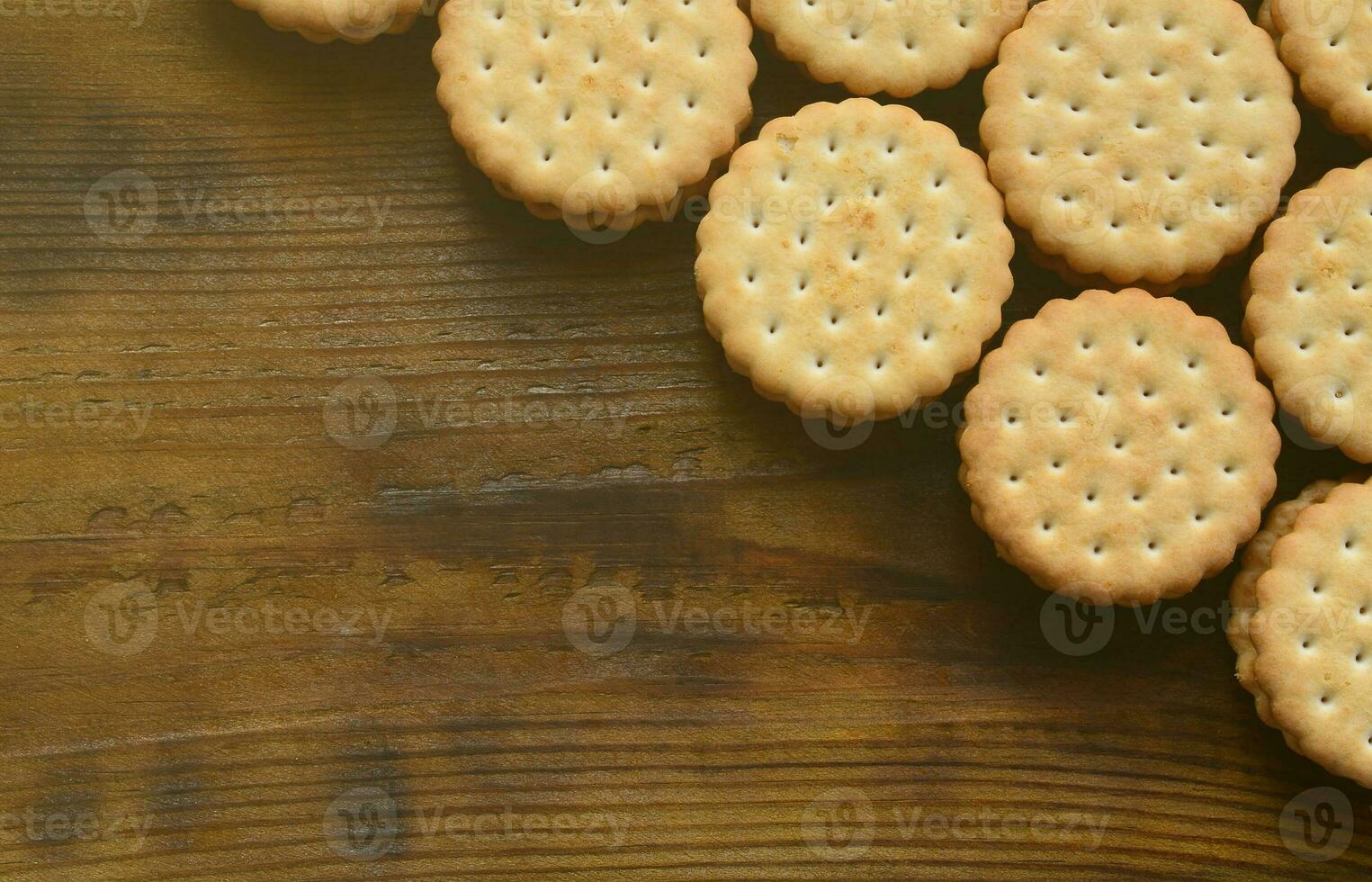 A round sandwich cookie with coconut filling lies in large quantities on a brown wooden surface. Photo of edible treats on a wooden background with copy space