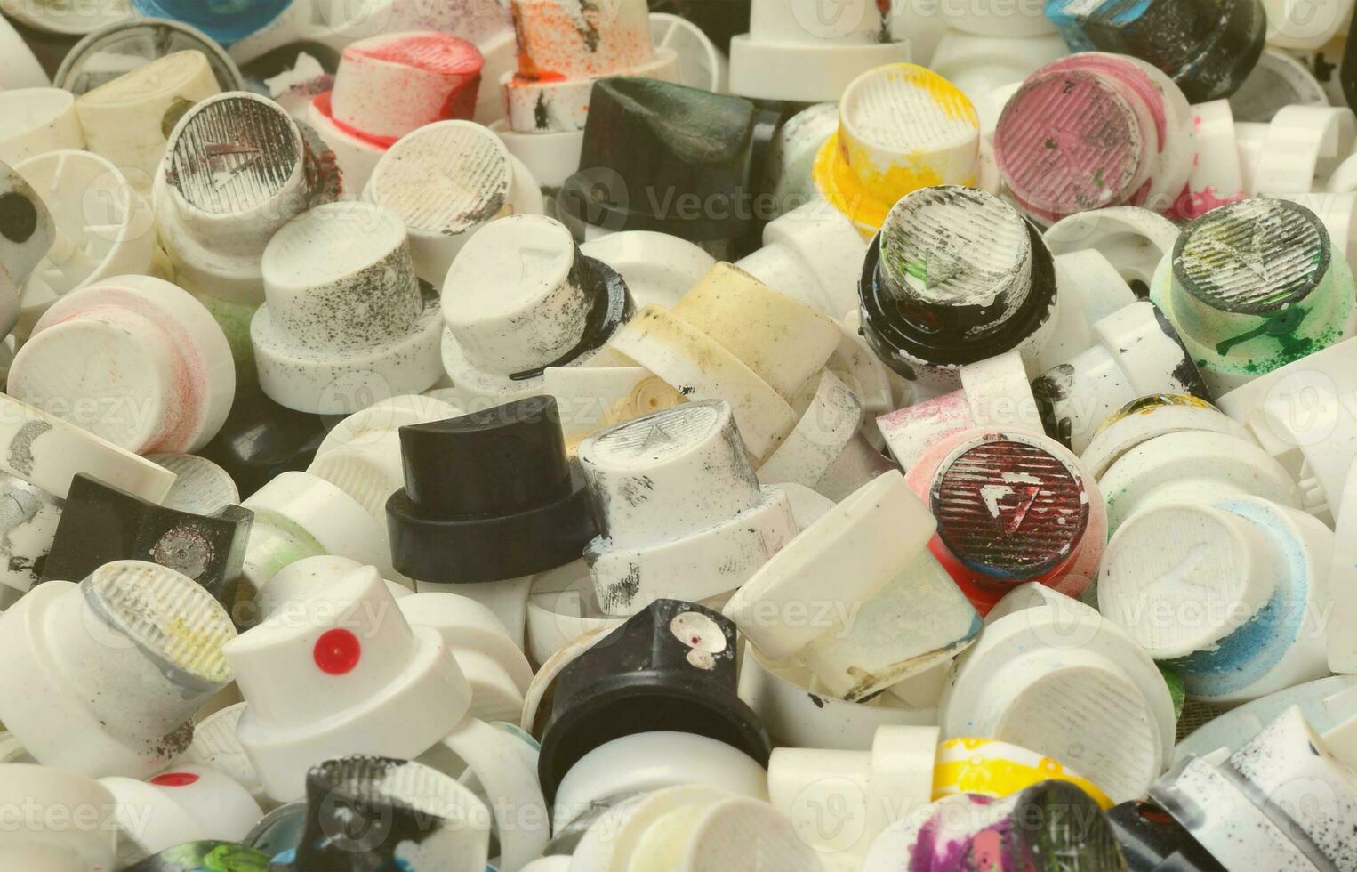 A large number of caps from cans of aerosol paint for graffiti. Smeared with colored paint nozzles lie in a huge pile photo