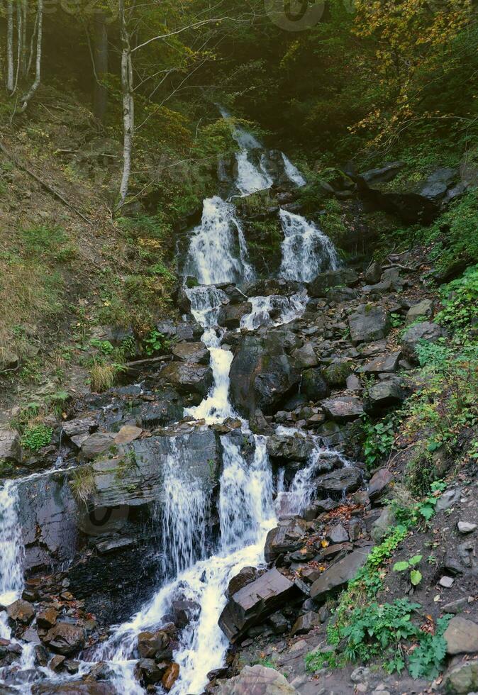 A mountain waterfall flows over the rocks. Waterfall cascade on mossy rocks photo