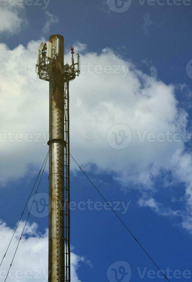 High metal chimney of industrial plant with ladder in the form of metal braces against the background of a cloudy blue sky photo