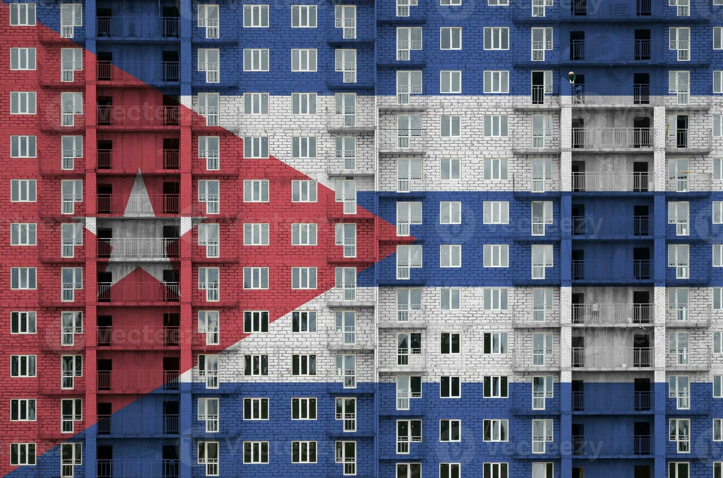 Cuba flag depicted in paint colors on multi-storey residental building under construction. Textured banner on brick wall background photo