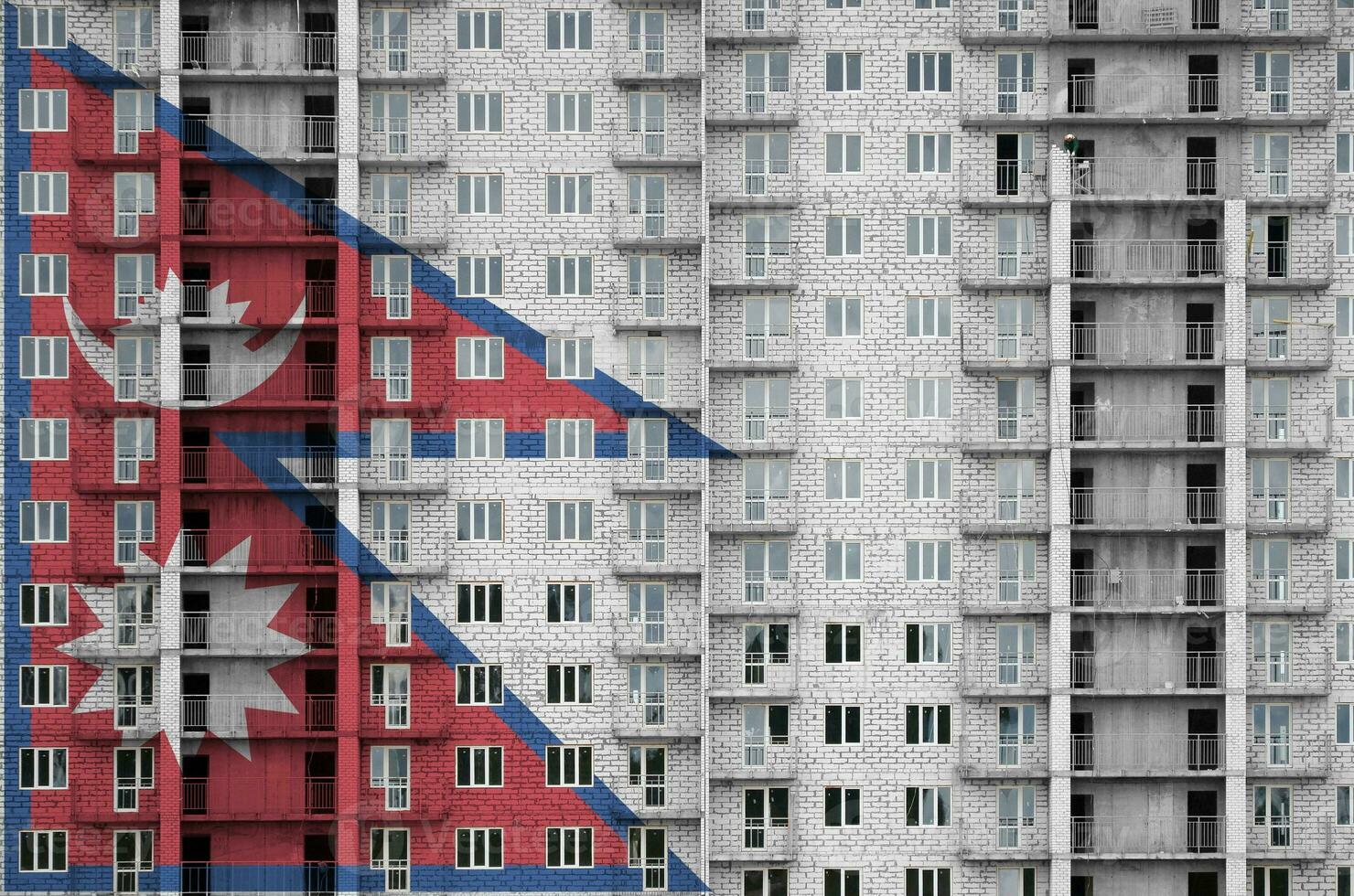 Nepal flag depicted in paint colors on multi-storey residental building under construction. Textured banner on brick wall background photo
