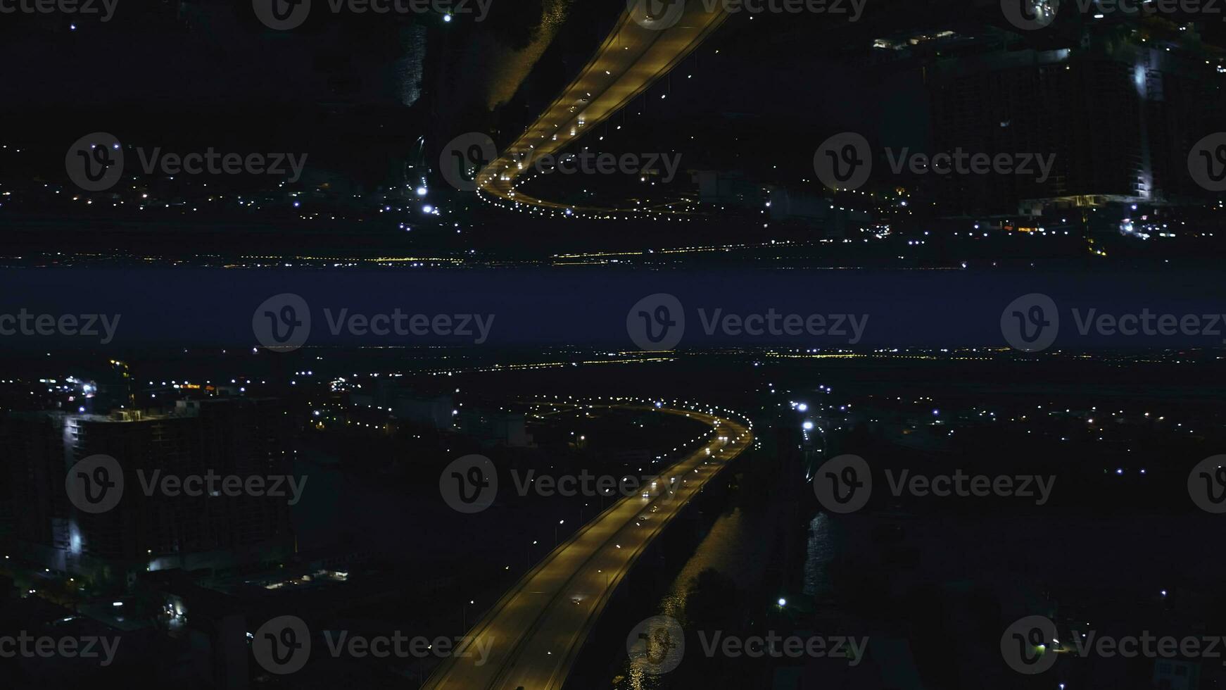 Aerial night view of a river bridge with moving cars and the city with night lights, mirror horizon effect. Media. Stunning landscape of night city and the bridge across the river, inception theme. photo