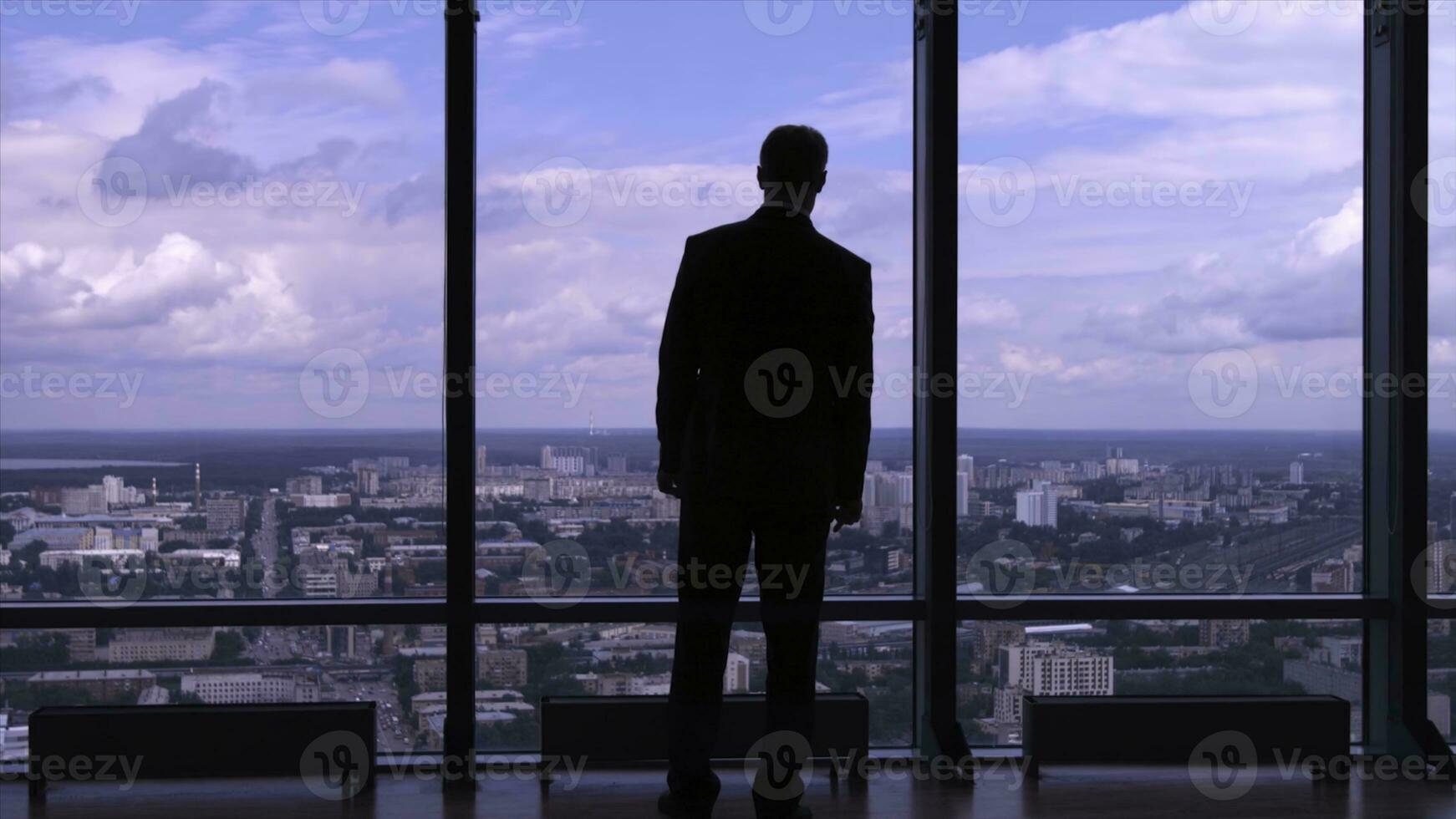 Businessman in suit standing next to a big window from an office building and checking his watch back view. Businessman standing at window looking on his wrist watch photo