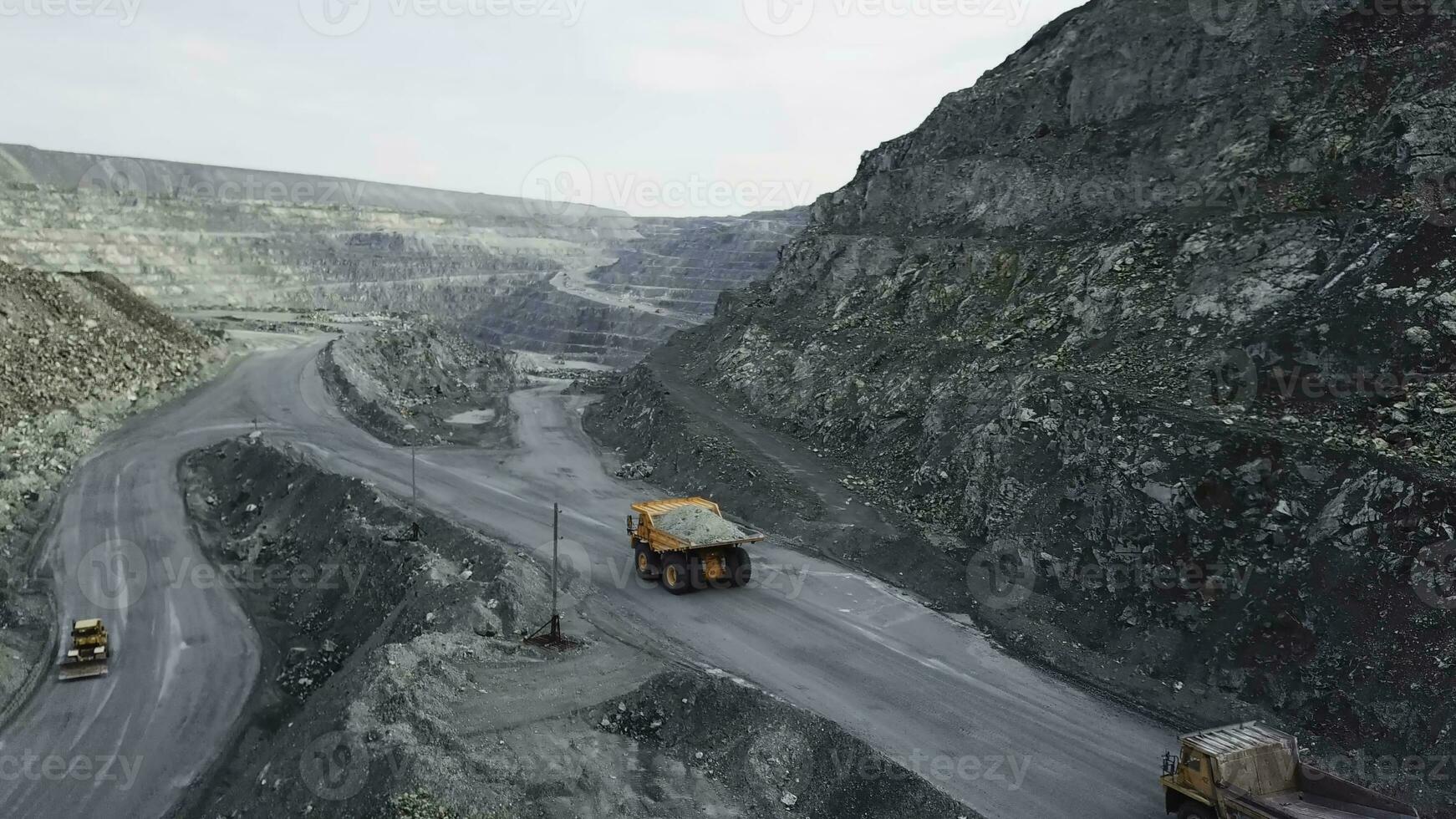 Dump truck is at quarry. Top view of driving orange dump truck with rubble on road open pit. Heavy transport in mining industry photo