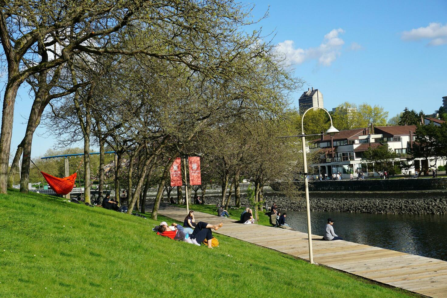 People enjoying a sunny spring day near the water in the park, with a stunning cityscape in the background. Vancouver, BC, Canada. May 02, 2021. photo