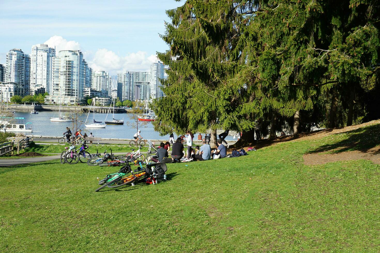 People enjoying a sunny spring day near the water in the park, with a stunning cityscape in the background. Vancouver, BC, Canada. May 02, 2021. photo