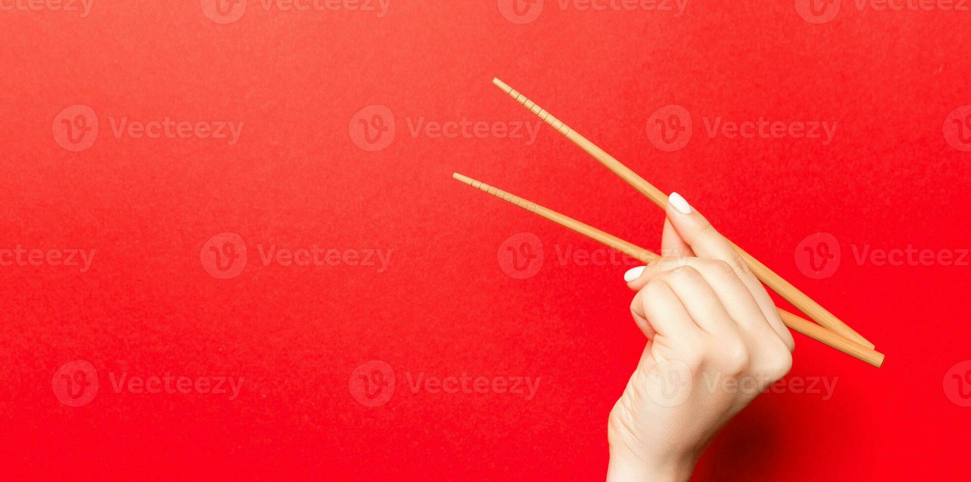 Creative image of wooden chopsticks in female hand on red background. Japanese and chinese food with copy space photo