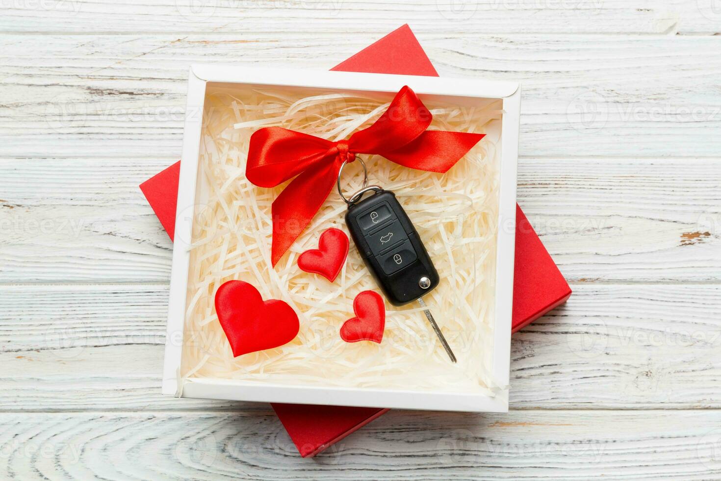 Black car key in a present box with a ribbon and red heart on colored background. Valentine day composition Top view photo