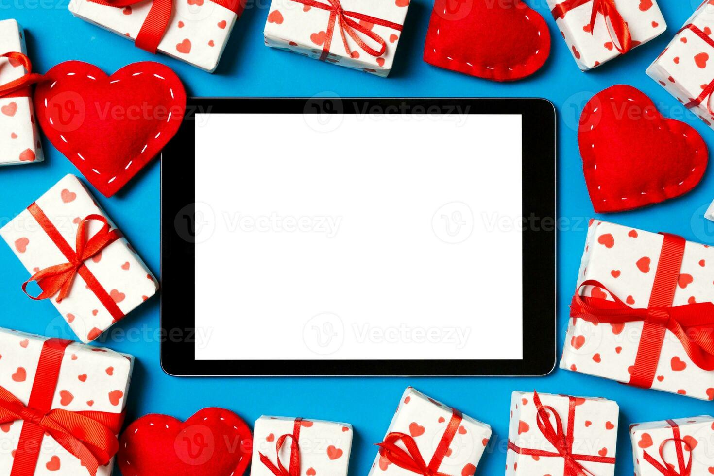 Top view of digital tablet surrounded with gift boxes and hearts on colorful background. Saint Valentine's day photo