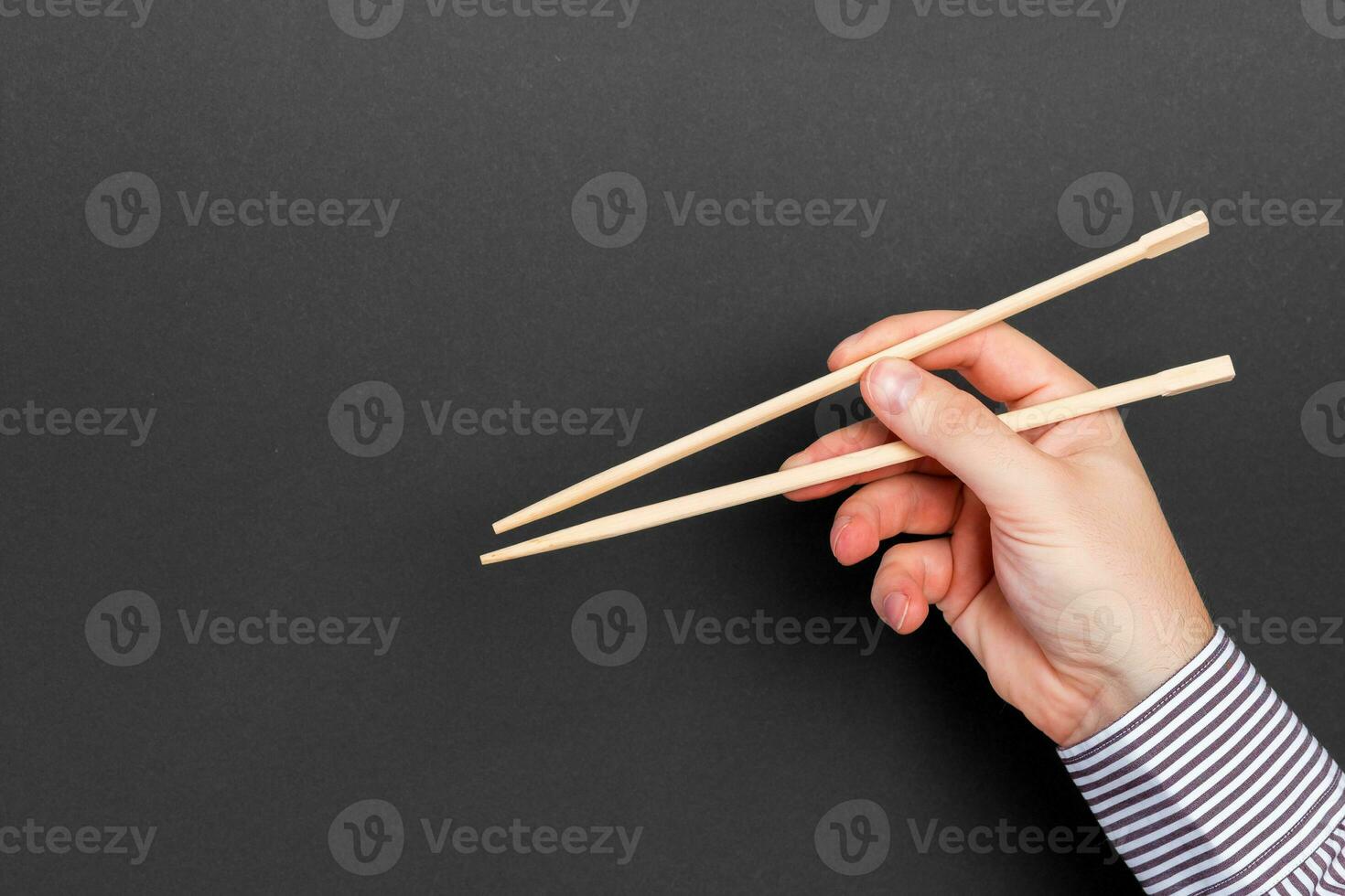 Male hand with chopsticks on black background. Traditional asian food with emty space for your design photo