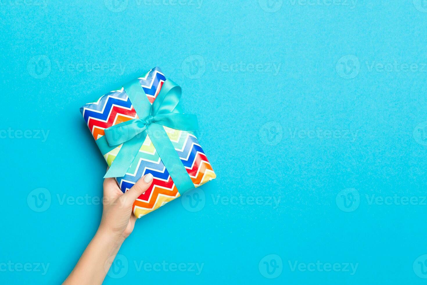 mujer brazos participación regalo caja con de colores cinta en azul mesa fondo, parte superior ver y Copiar espacio para usted diseño foto