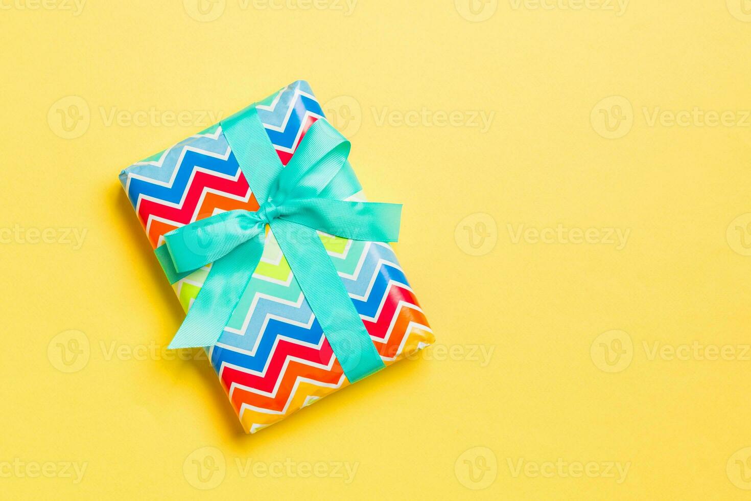 Gift box with blue bow for Christmas or New Year day on yellow background, top view with copy space photo