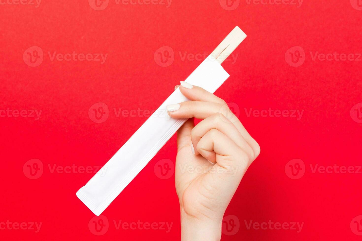 Woman's hand holding chopsticks in a pack on red background. Chinese food concept with empty space for your design photo