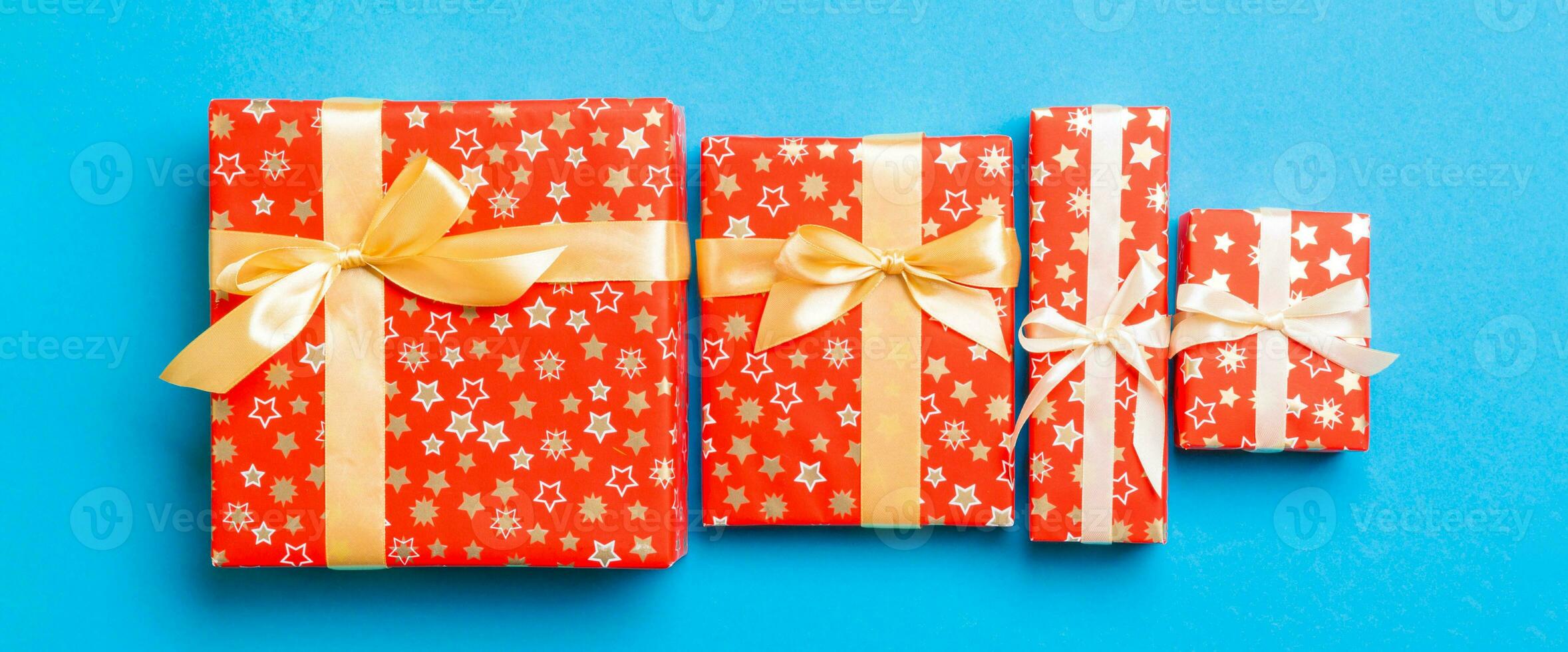 wrapped Christmas or other holiday handmade present in paper with gold ribbon on blue background. Present box, decoration of gift on colored table, top view photo