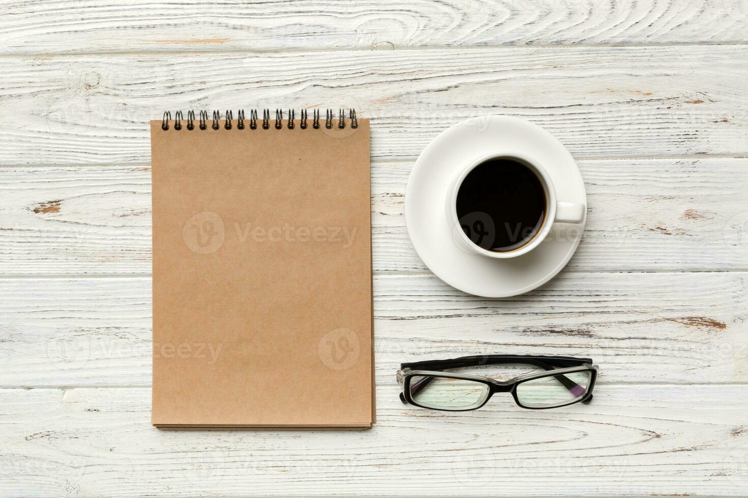 Modern office desk table with notebook and other supplies with cup of coffee. Blank notebook page for you design. Top view, flat lay photo