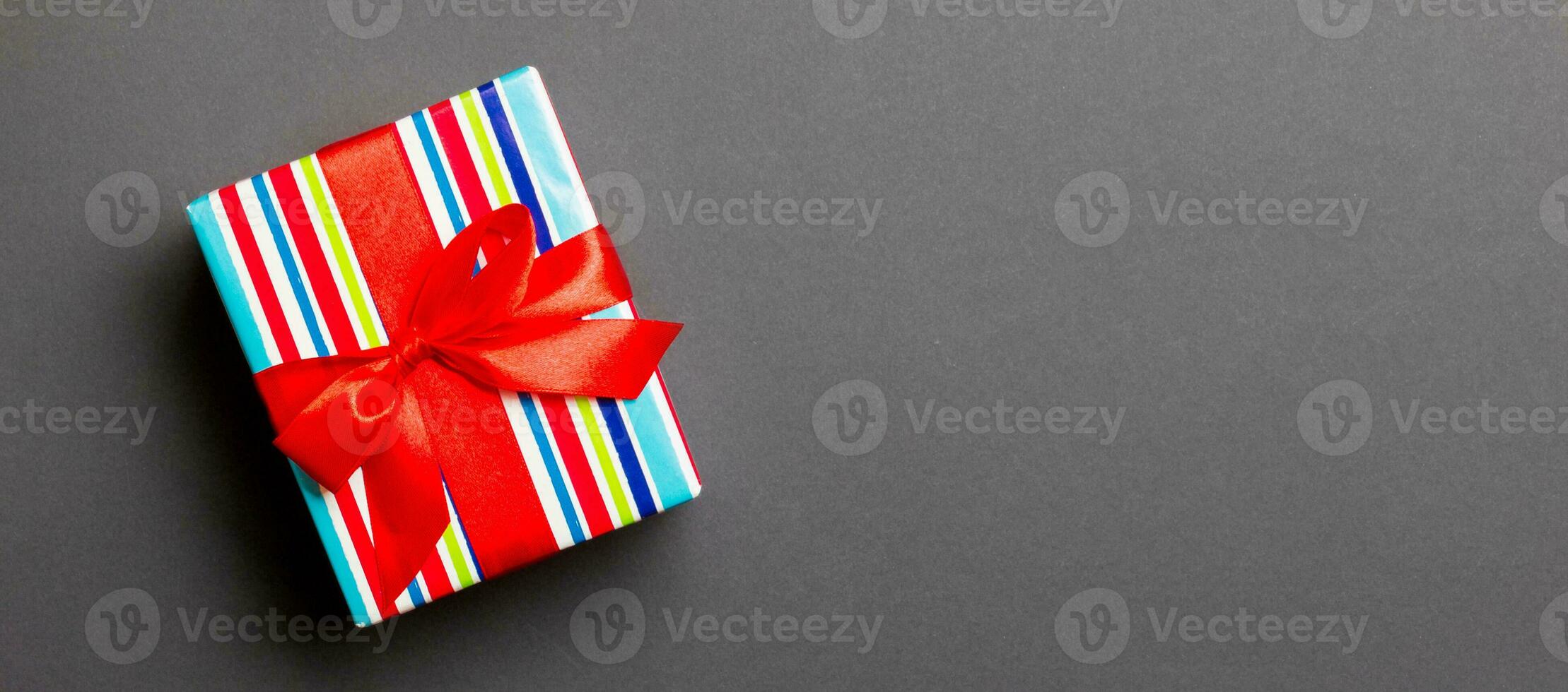 wrapped Christmas or other holiday handmade present in paper with red ribbon on black background. Present box, decoration of gift on colored table, top view with copy space photo
