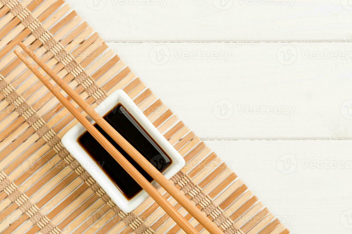 Bamboo mat and soy sauce with sushi chopsticks on white wooden table. Top view with copy space background for sushi. Flat lay photo