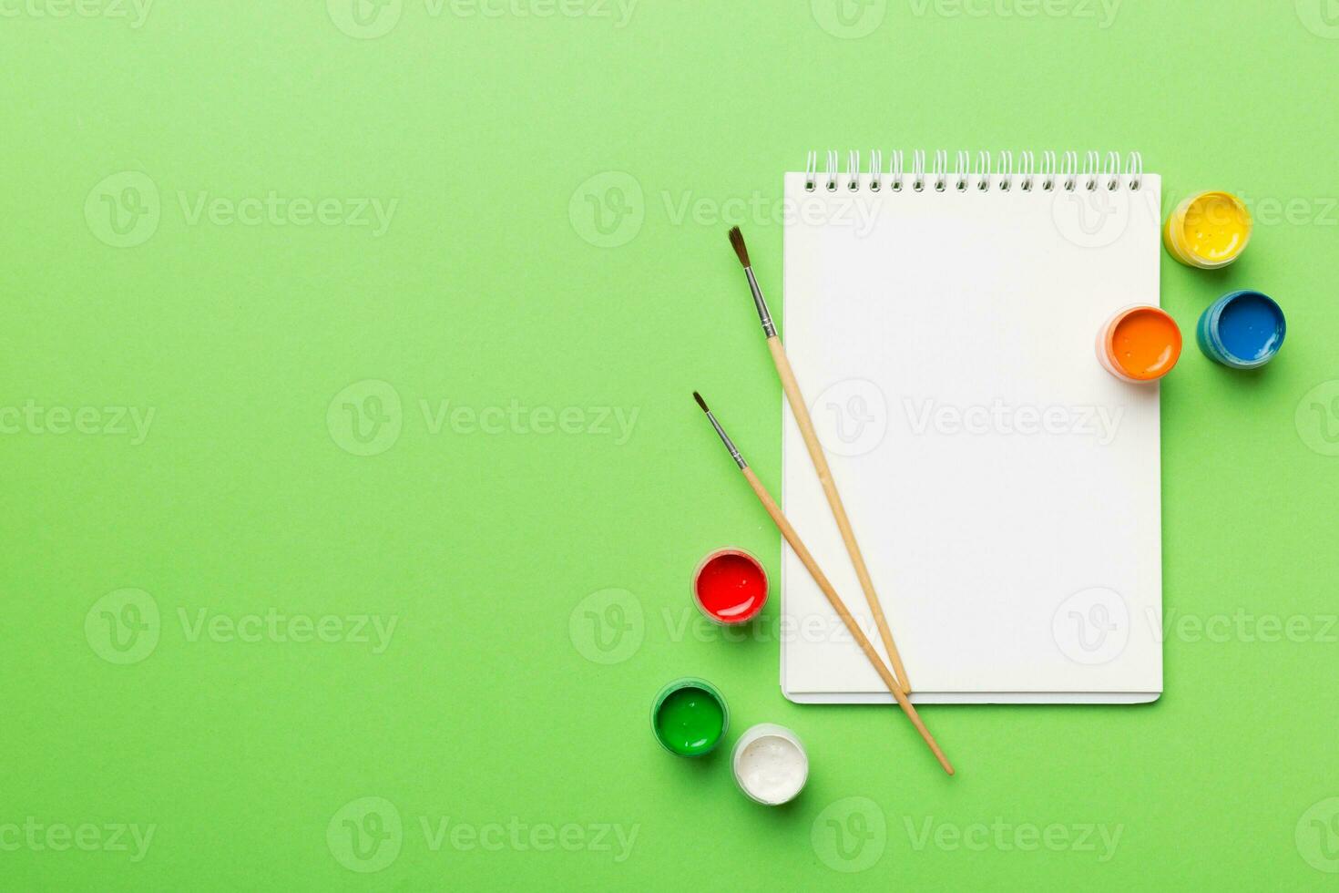 Album pages and paints, pencils, brush on a colored background. Top view with empty space. workplace for creativity. home teaching concept drawing photo