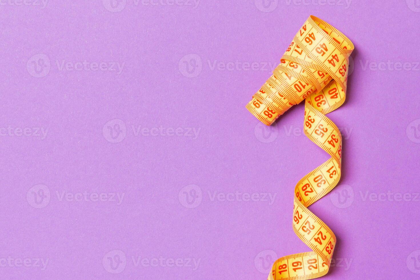 Top view of curled measuring tape as a sewing accessory on purple background. Tailor concept with copy space photo