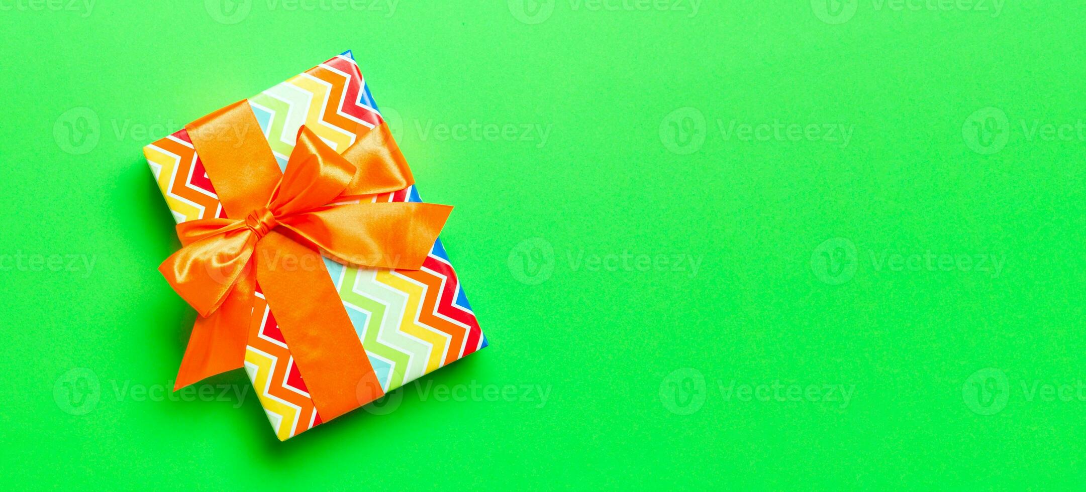 Top view Christmas present box with orange bow on green background with copy space photo