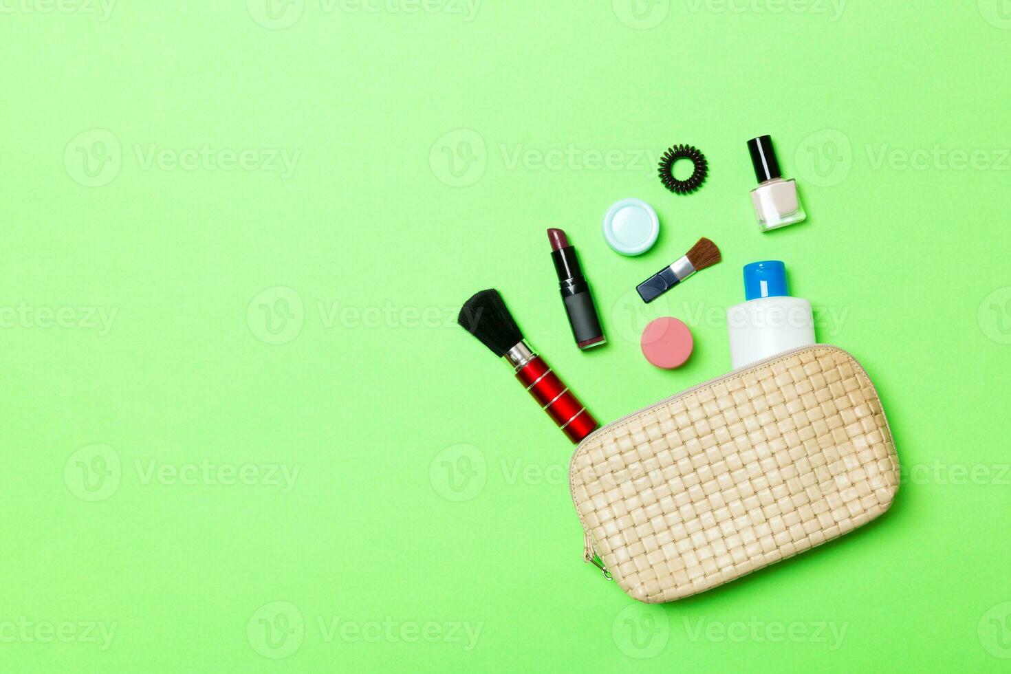 Aerial view of a leather cosmetics bag with make up beauty products spilling out on green background. Beautiful skin concept with copy space photo