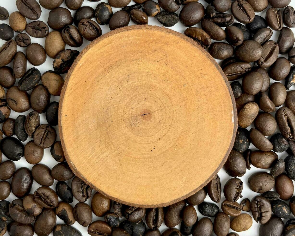 Empty copy spaced wooden coaster platform with black whole raw aromatic coffee beans on the background. Rustic warm toned image. Bitter drink ingredients with Caffeine. Genus Coffea, Rubiaceae family. photo