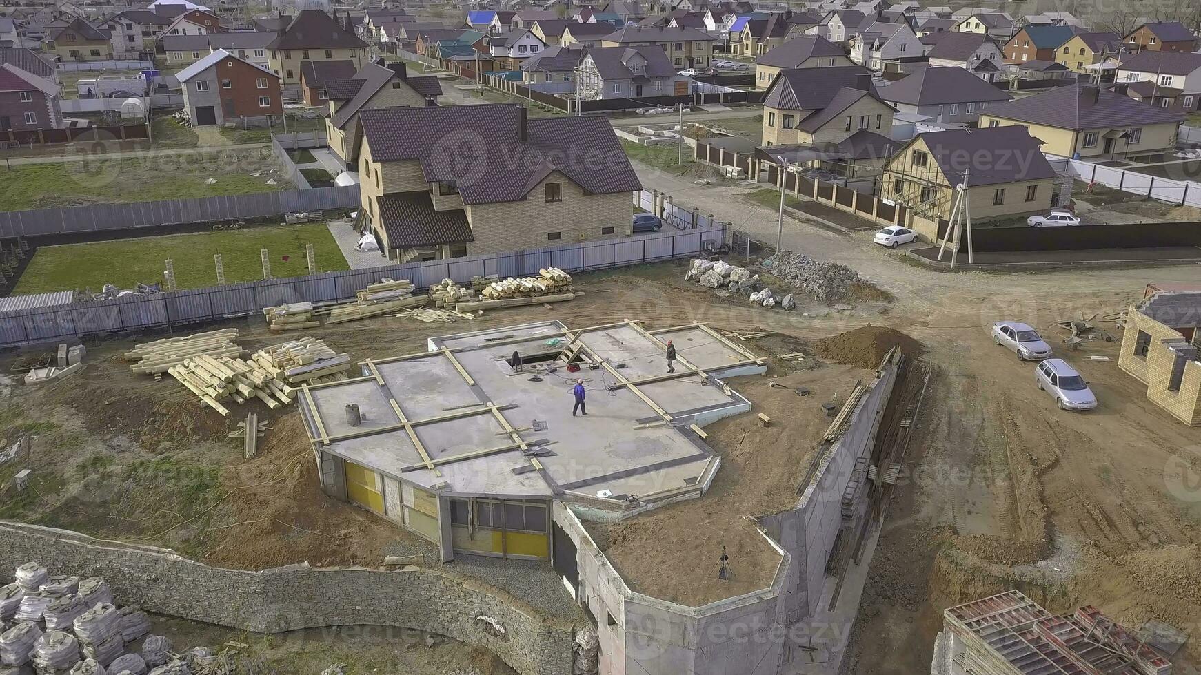 Top view of concrete base of house. Clip. Workers at construction site check concrete base of house under construction on background of country cottages photo