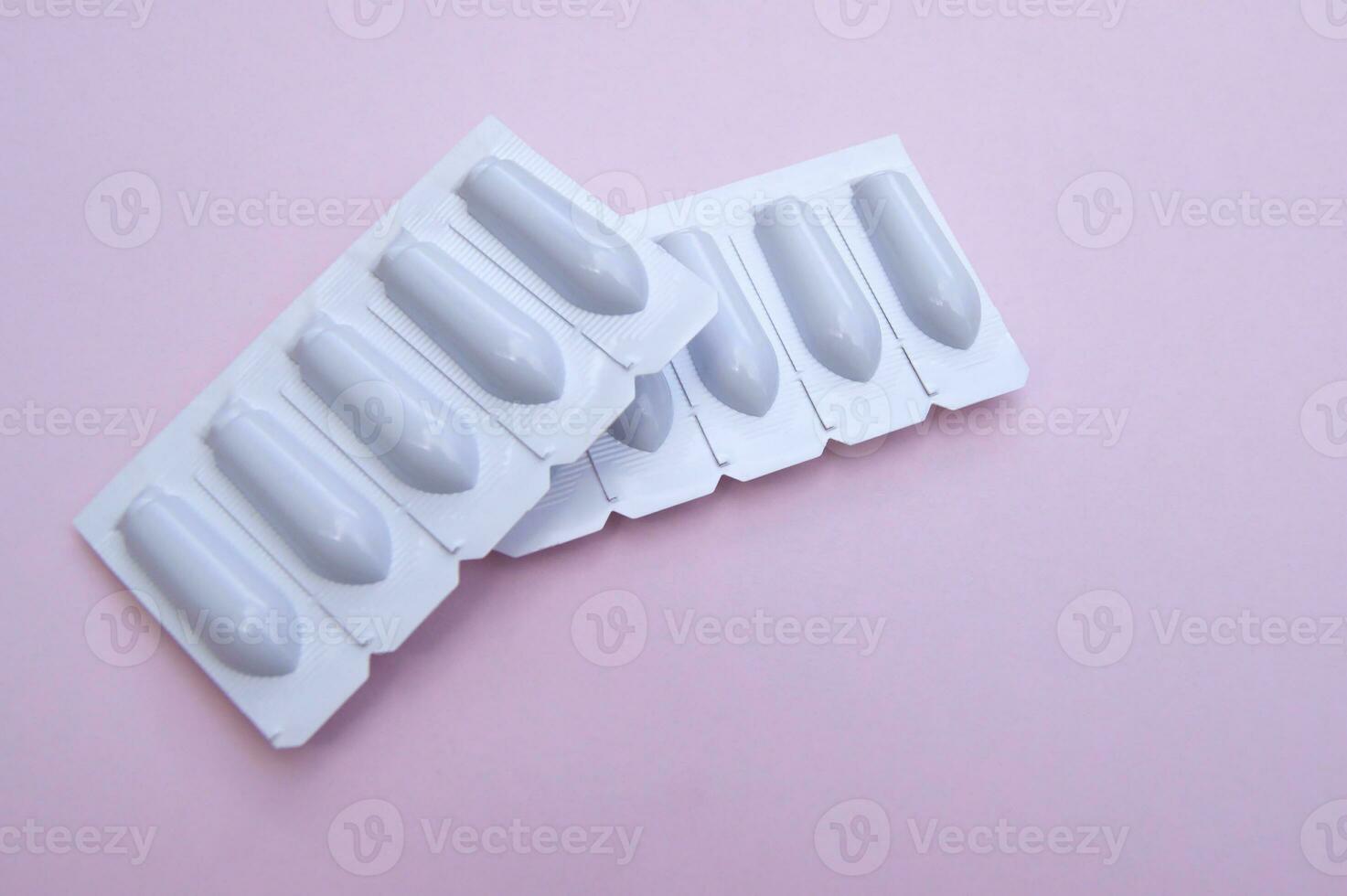 Gynecological medicines for women's health in form of suppository, capsules on pink background. photo