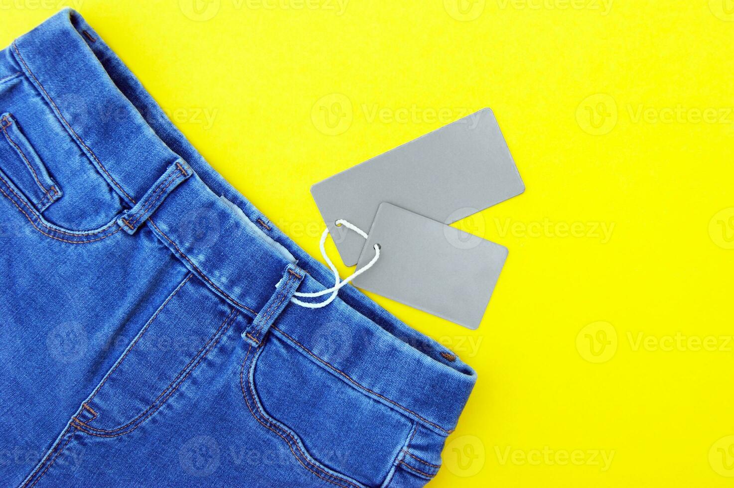 Flat lay, detail of jeans, blank grey labels on yellow background. photo