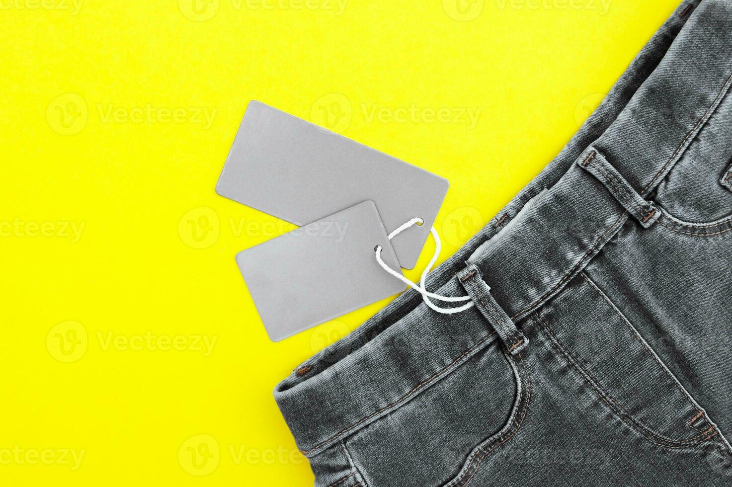 Flat lay, detail of black jeans, blank grey labels on yellow background. photo