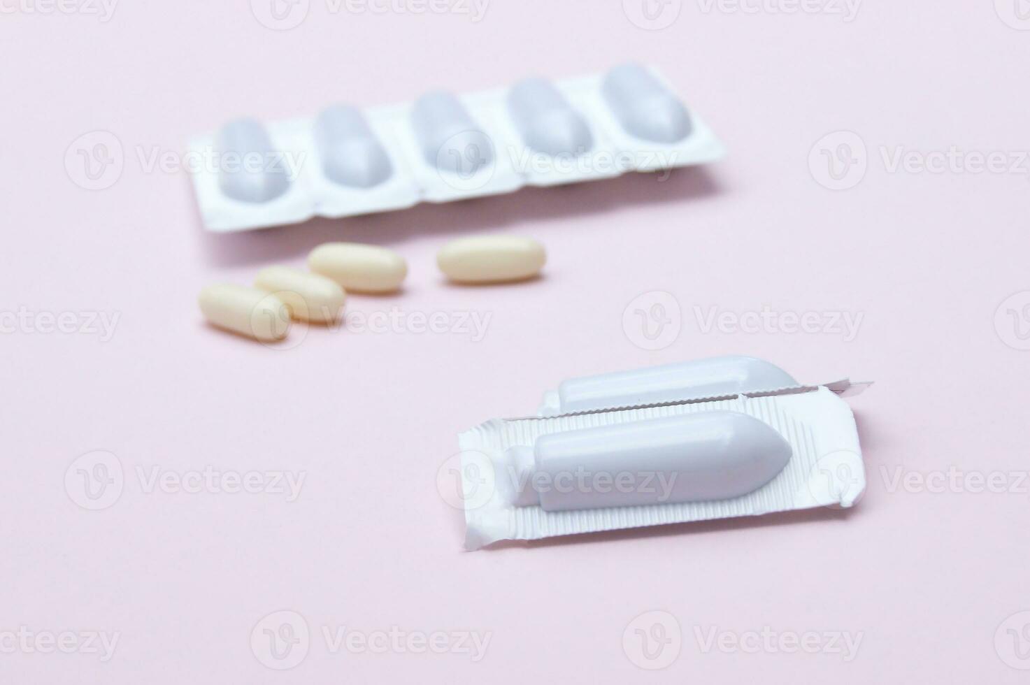 Gynecological medicines for women's health in form of suppository, capsules on pink background. photo