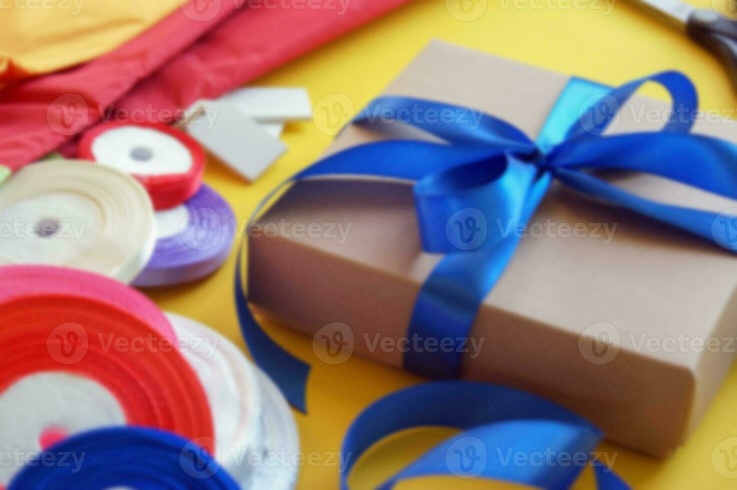 Gift box packaging on a yellow background. A lot of bright satin ribbons. photo