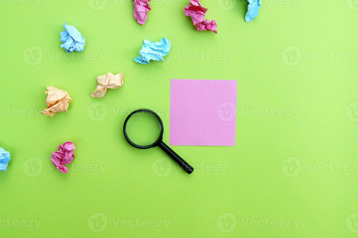 Top view photo of a magnifying glass and blank sticker on a green background.