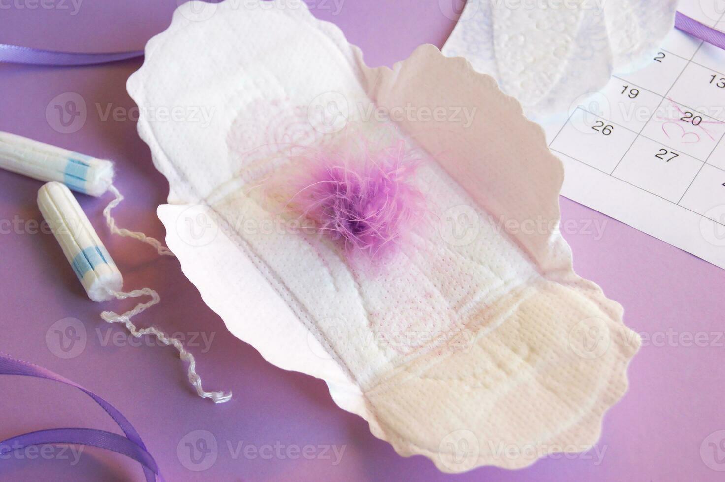 Menstrual pads and tampons on menstruation period calendar with on lilac background. photo